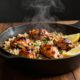 Golden chicken thighs and creamy rice sit in a cast-iron skillet with lemon wedges.