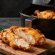 Sliced crispy chicken breast with lemon, rosemary, and an open air fryer basket.