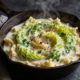 A skillet of creamy cabbage Alfredo topped with parsley and pepper on a dark slate surface.