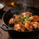 Honey garlic chicken in a skillet with rice, garlic, sesame seeds, and green onions.